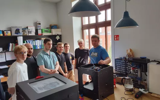 Mgr inż. Karol Kropidłowski wraz z grupą studentów omawiają konstrukcję drukarki 3D oraz istotne aspekty związane z procesem druku.